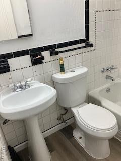 full bathroom featuring toilet, shower / washtub combination, wood finished floors, and tile walls