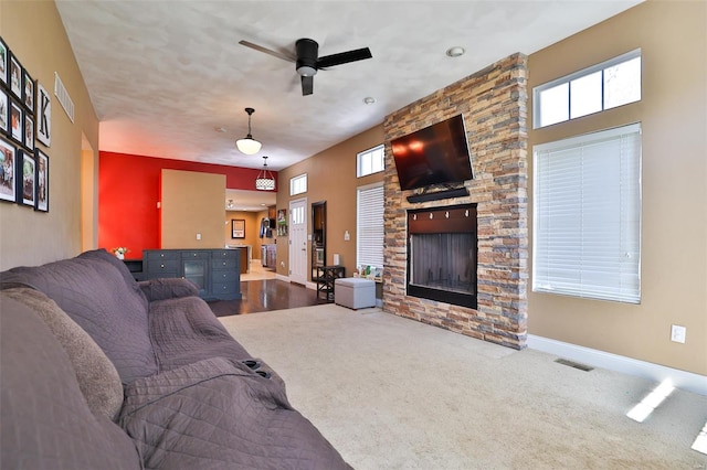 living area with visible vents, ceiling fan, a stone fireplace, and carpet floors