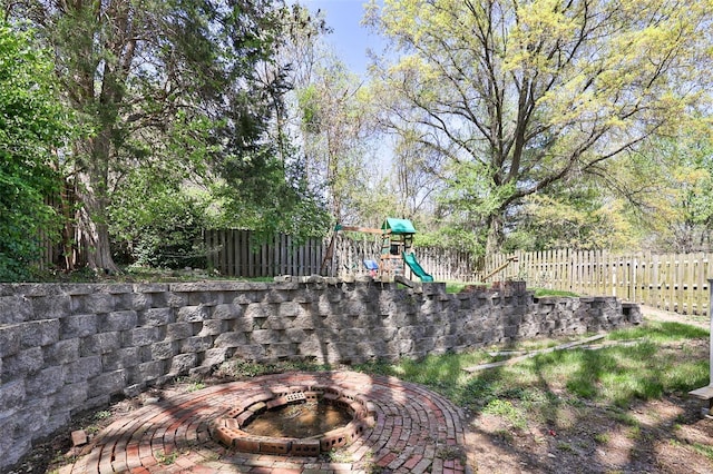 view of yard with a fire pit, a fenced backyard, and a playground