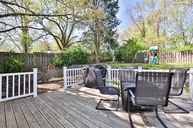 deck with outdoor dining space, a playground, and a fenced backyard