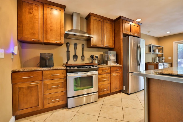 kitchen featuring light stone countertops, brown cabinets, light tile patterned floors, wall chimney range hood, and appliances with stainless steel finishes