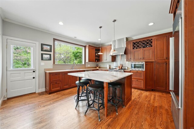 kitchen featuring a kitchen breakfast bar, crown molding, a sink, stainless steel microwave, and wall chimney exhaust hood