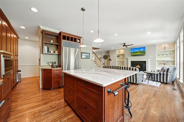 kitchen with a breakfast bar, a warm lit fireplace, light wood-style flooring, hanging light fixtures, and ceiling fan