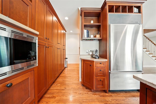 kitchen with open shelves, brown cabinets, light wood-style floors, stainless steel appliances, and light countertops