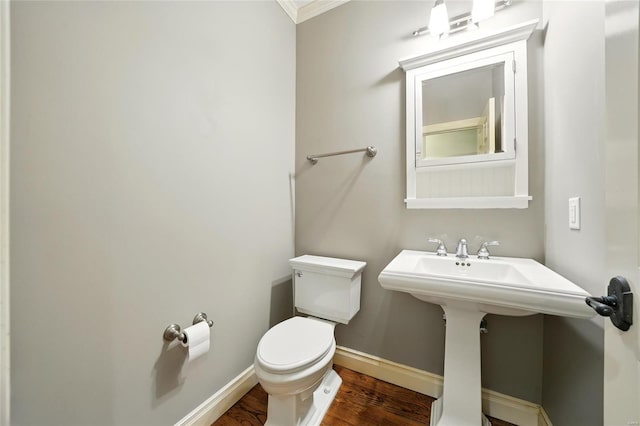 half bathroom featuring a sink, toilet, baseboards, wood finished floors, and crown molding