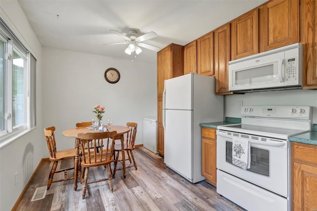 kitchen featuring brown cabinetry, a ceiling fan, visible vents, light wood finished floors, and white appliances