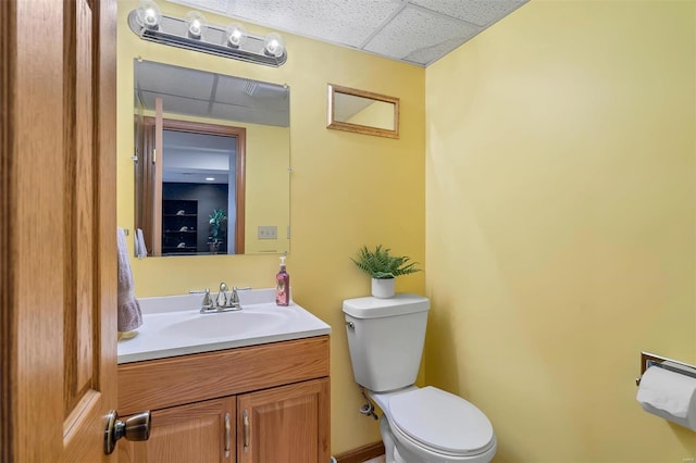 half bath featuring vanity, a drop ceiling, and toilet
