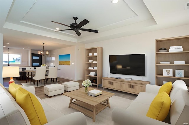 living area featuring built in shelves, recessed lighting, light wood finished floors, and a raised ceiling