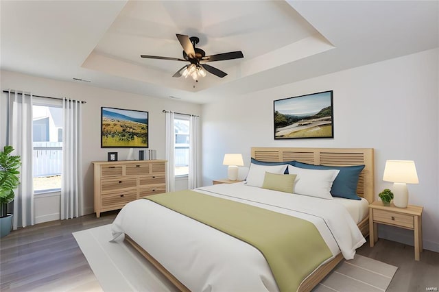 bedroom with wood finished floors, a tray ceiling, and baseboards