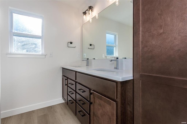full bathroom featuring double vanity, a sink, wood finished floors, and baseboards