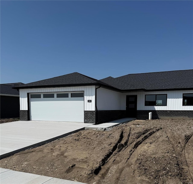 prairie-style home with driveway, roof with shingles, an attached garage, and brick siding