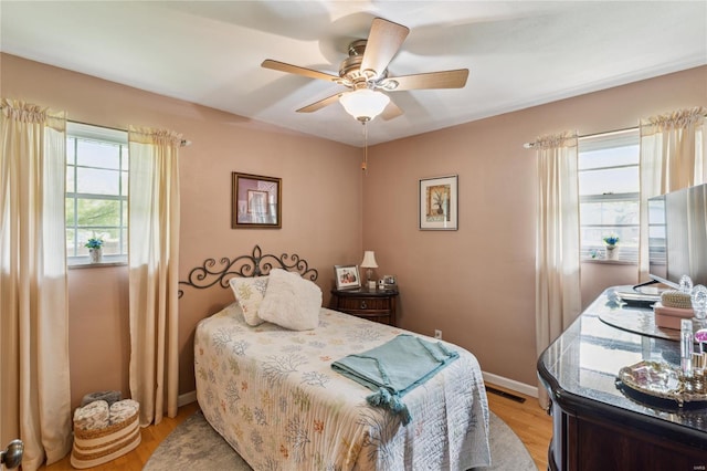 bedroom with light wood-style floors, a ceiling fan, visible vents, and baseboards