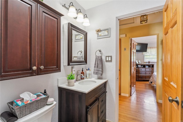 bathroom with toilet, vanity, wood finished floors, and baseboards