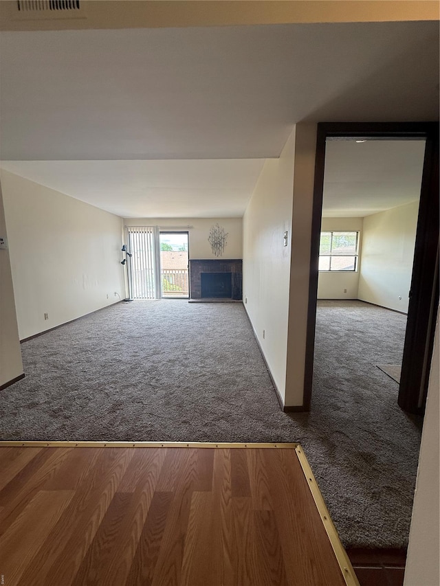 unfurnished living room with carpet floors, a tiled fireplace, and a wealth of natural light