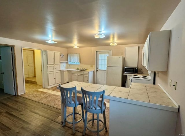 kitchen with a peninsula, tile counters, white appliances, and a sink