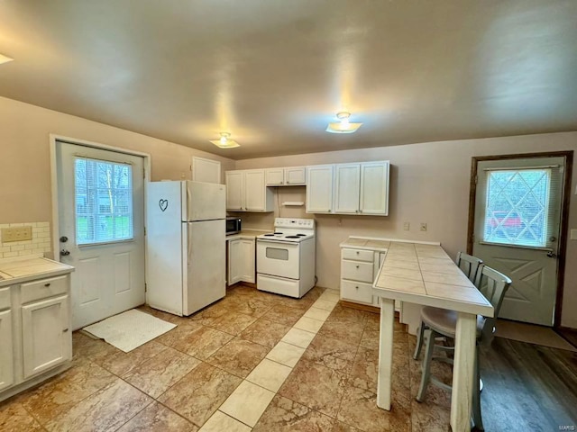 kitchen featuring tile countertops, backsplash, white appliances, and white cabinets