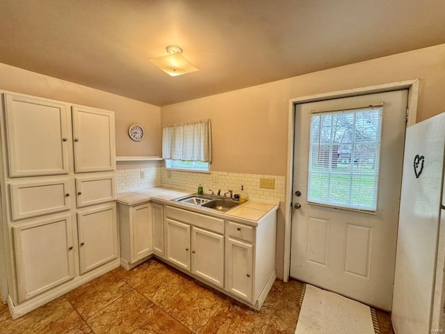kitchen featuring a sink, white cabinets, tile countertops, backsplash, and freestanding refrigerator