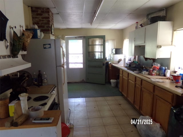 kitchen with light countertops, a drop ceiling, range hood, and a sink