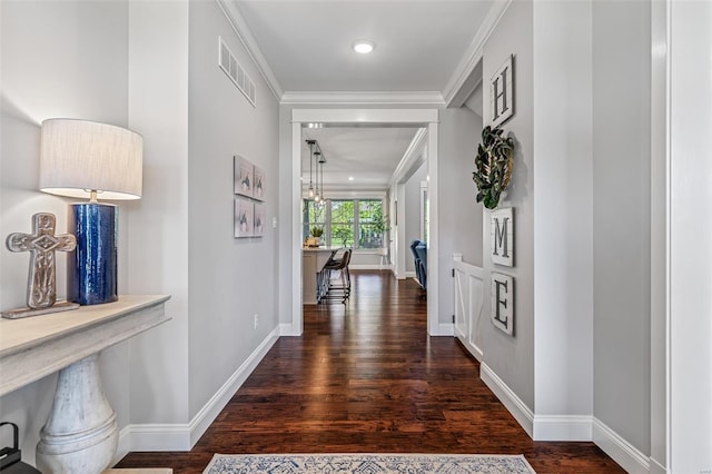 hallway featuring baseboards, wood finished floors, visible vents, and ornamental molding