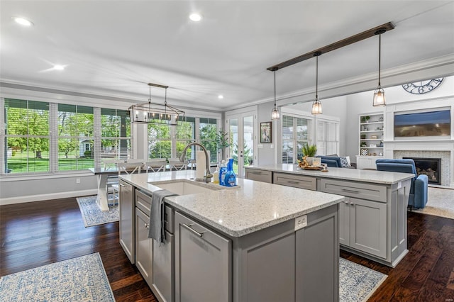 kitchen with gray cabinets, ornamental molding, and a center island with sink
