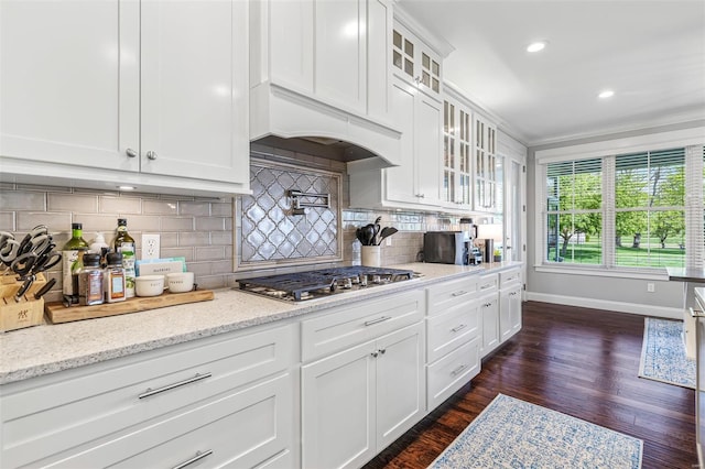kitchen with stainless steel gas stovetop, decorative backsplash, glass insert cabinets, dark wood finished floors, and baseboards