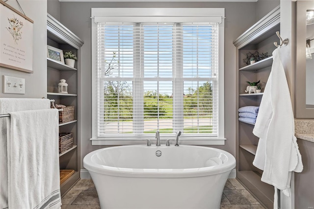bathroom with a soaking tub, plenty of natural light, and stone tile floors