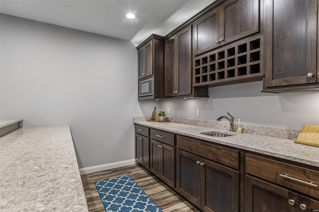 kitchen featuring dark brown cabinets, a sink, stainless steel microwave, baseboards, and dark wood-type flooring