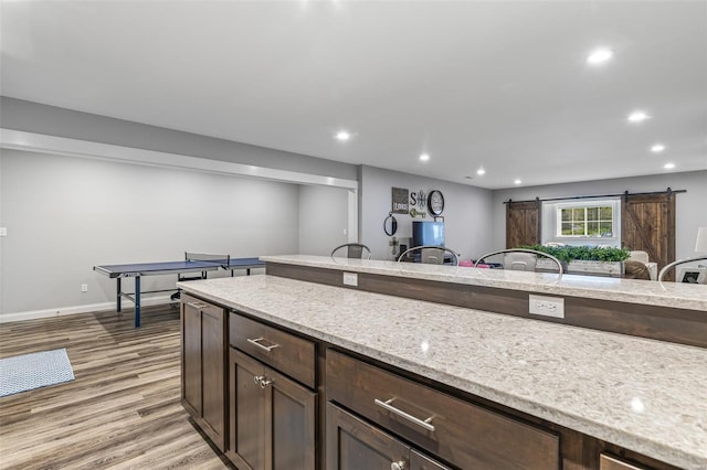 kitchen with dark brown cabinetry, light wood-style flooring, baseboards, light stone countertops, and recessed lighting
