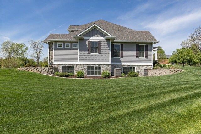 rear view of property featuring a yard, stone siding, and a shingled roof