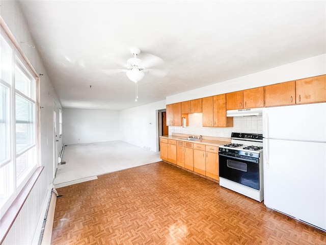 kitchen with a sink, freestanding refrigerator, backsplash, range with gas stovetop, and under cabinet range hood
