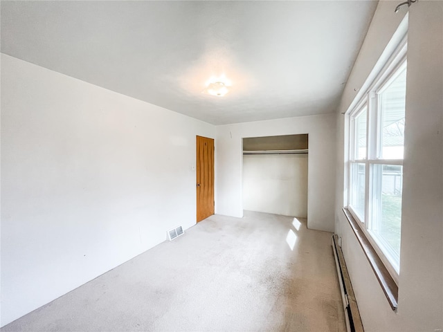 unfurnished bedroom featuring a baseboard heating unit, visible vents, and a closet