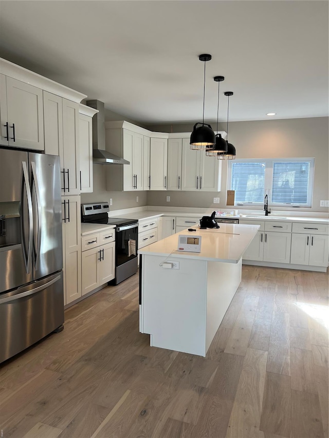 kitchen with wall chimney range hood, a center island, light countertops, stainless steel appliances, and light wood-style flooring