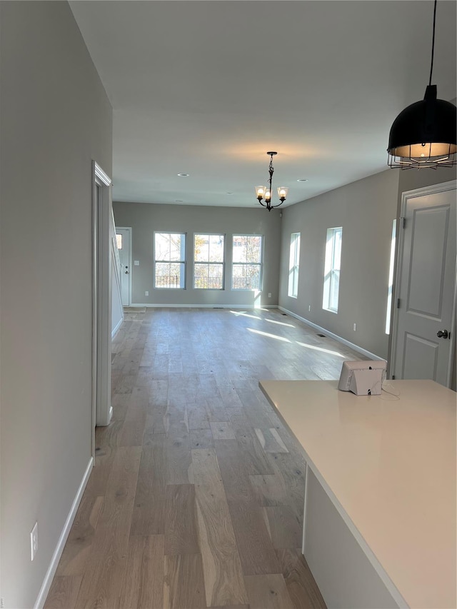 unfurnished dining area with baseboards, an inviting chandelier, and light wood finished floors