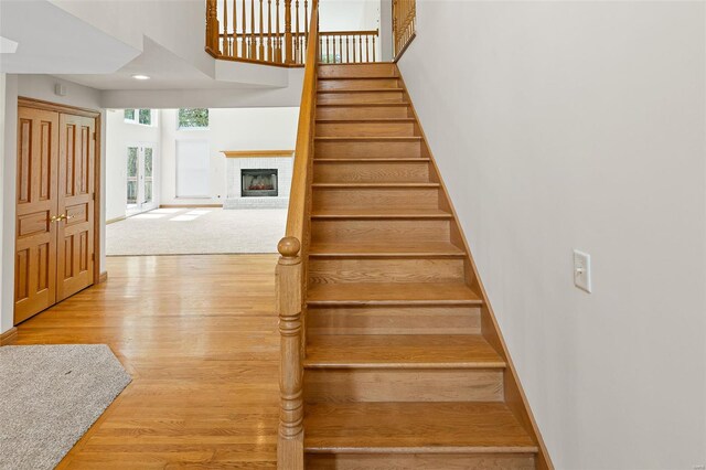 staircase featuring a high ceiling, a brick fireplace, wood finished floors, and baseboards