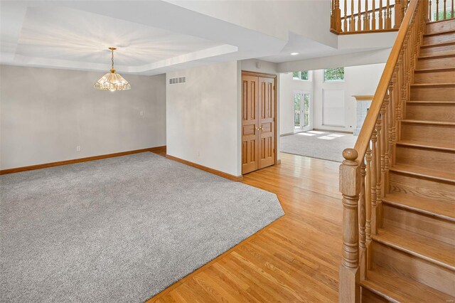 empty room with light wood-style flooring, visible vents, baseboards, an inviting chandelier, and stairway