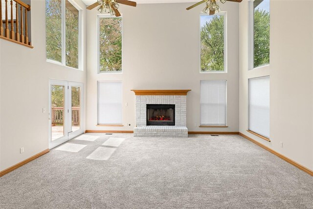 unfurnished living room featuring ceiling fan, carpet flooring, a towering ceiling, and a brick fireplace