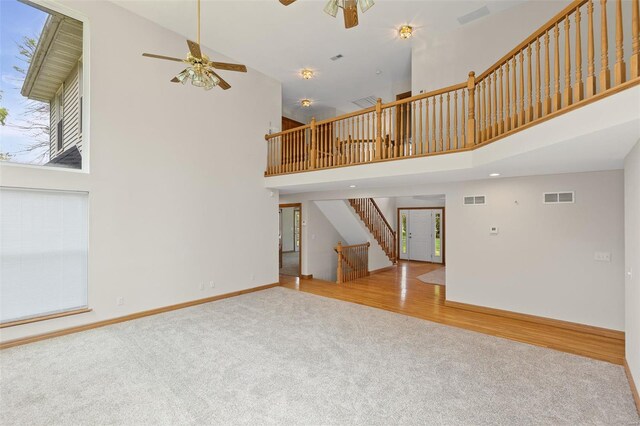 unfurnished living room featuring carpet, a high ceiling, visible vents, a ceiling fan, and stairs