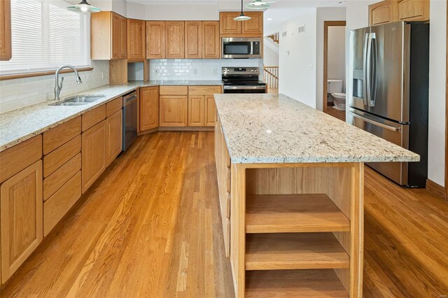 kitchen featuring a center island, a sink, light wood-type flooring, light stone countertops, and appliances with stainless steel finishes