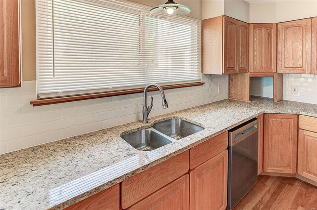 kitchen with light wood finished floors, a sink, backsplash, light stone counters, and dishwasher