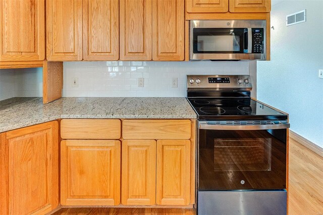 kitchen with light wood-style floors, backsplash, appliances with stainless steel finishes, light stone countertops, and visible vents