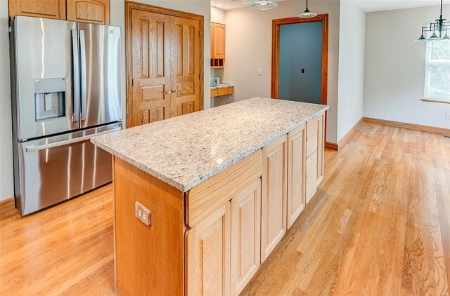 kitchen with light stone counters, stainless steel fridge with ice dispenser, light wood-type flooring, a kitchen island, and hanging light fixtures