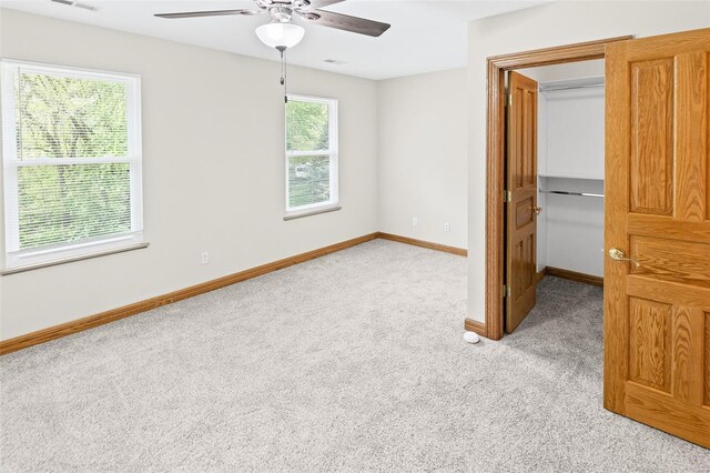 unfurnished bedroom featuring light carpet, baseboards, a spacious closet, a ceiling fan, and a closet