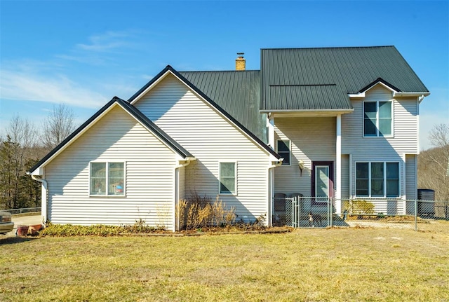 back of house featuring a chimney, fence, metal roof, and a yard