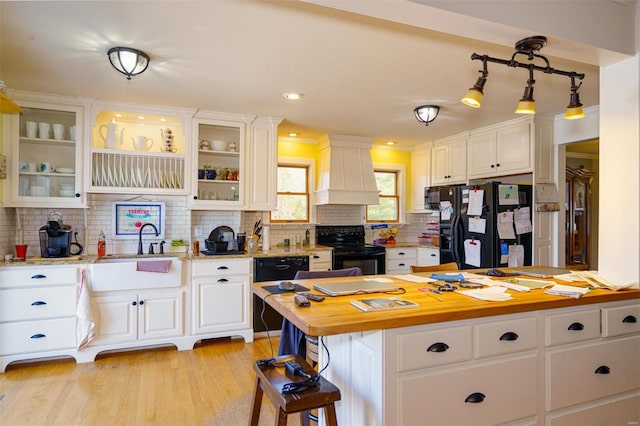 kitchen with black appliances, white cabinets, premium range hood, and backsplash
