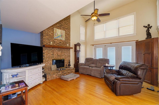 living area with high vaulted ceiling, wood finished floors, ceiling fan, and a brick fireplace
