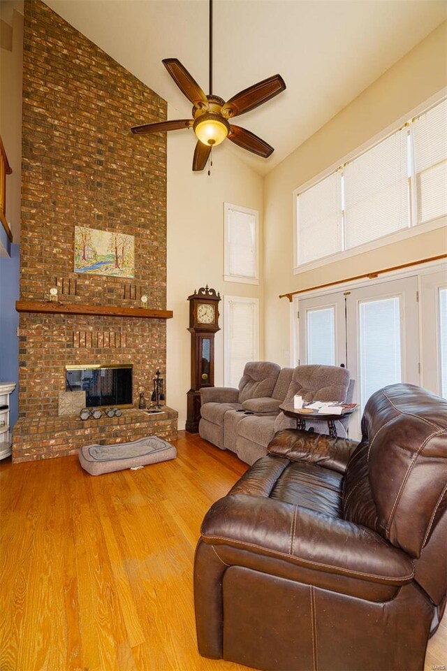 living area featuring a brick fireplace, a ceiling fan, high vaulted ceiling, and wood finished floors
