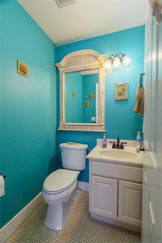 half bath featuring vanity, tile patterned floors, toilet, visible vents, and baseboards