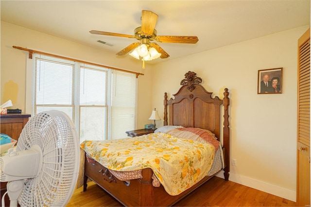 bedroom with wood finished floors, a ceiling fan, visible vents, and baseboards