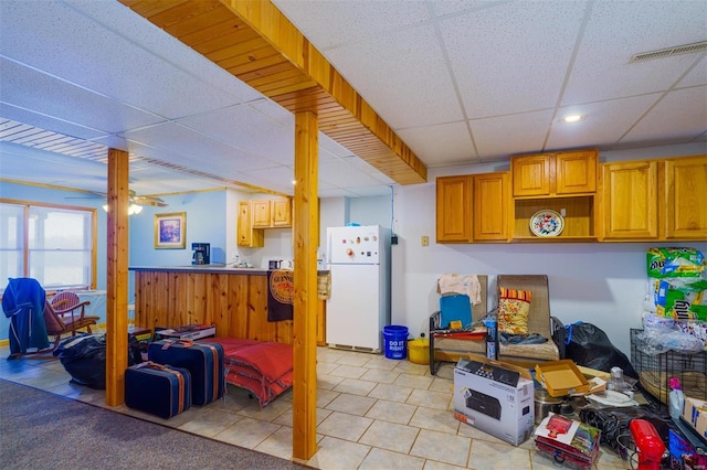 basement with recessed lighting, light tile patterned floors, visible vents, freestanding refrigerator, and a drop ceiling