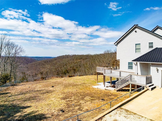 view of yard featuring a deck, fence, and a view of trees
